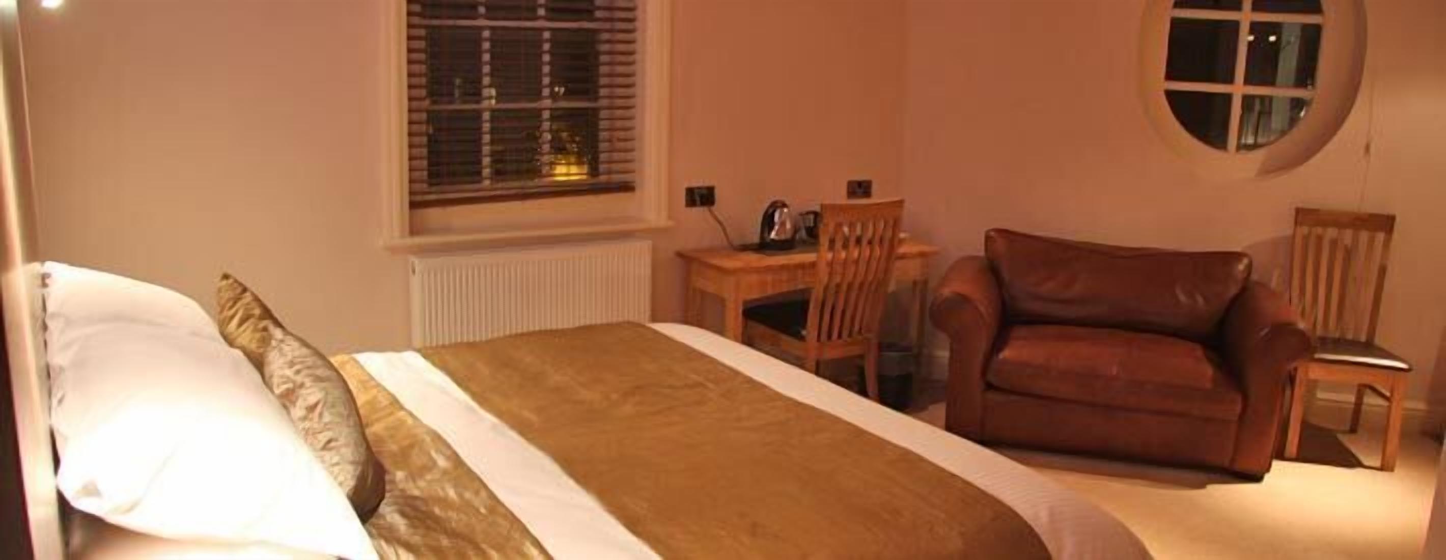 Een slaapkamer met een bed, een houten bureau, een leren fauteuil en een rond raam.