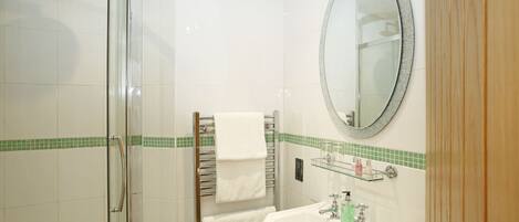 A bathroom with a glass shower enclosure, a white sink with a green soap dispenser, and a mirror with a decorative frame.