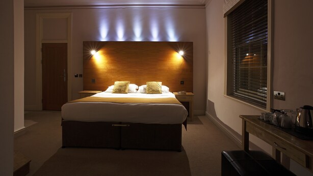 A hotel room with a large bed, bedside tables, a wooden headboard, and a window with blinds. - Castle Hotel (Aberystwyth)