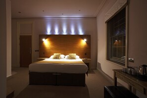 Una habitación de hotel con una cama grande, mesitas de noche, un cabecero de madera y una ventana con persianas.