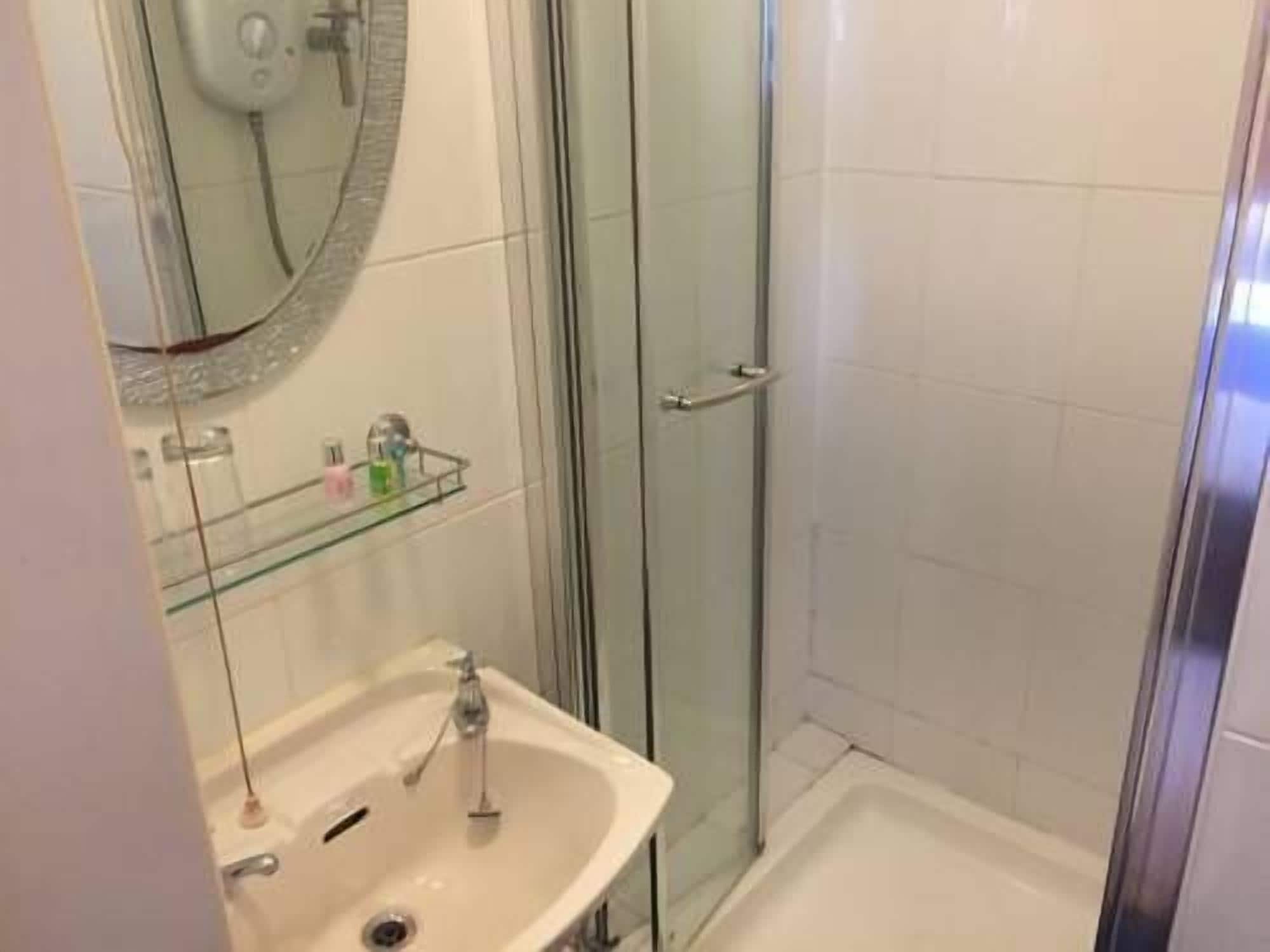 Un baño con cabina de ducha de vidrio, un lavabo con espejo y un estante de vidrio con artículos de aseo.