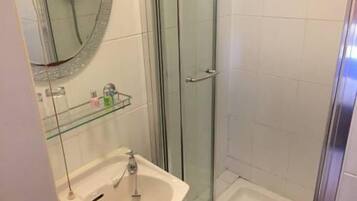 Un baño con cabina de ducha de vidrio, un lavabo con espejo y un estante de vidrio con artículos de aseo.