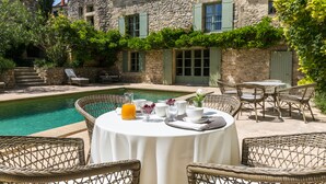A stone building with a pool, wicker furniture, and outdoor dining setup.