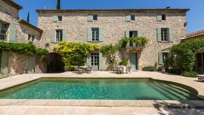 A stone building with a pool, outdoor seating, and a clear blue sky.