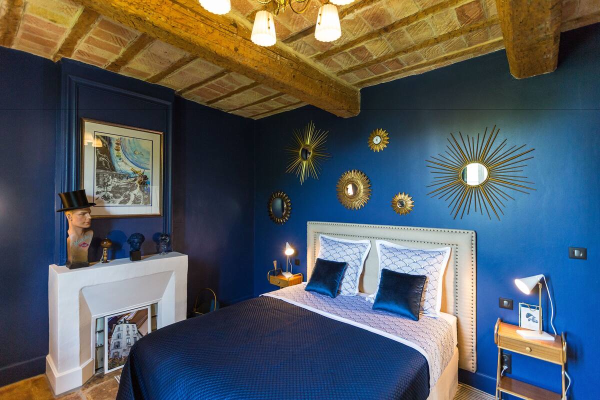Une chambre à coucher avec un grand lit, une cheminée et des œuvres d’art décoratives au mur.