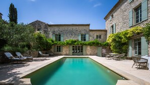 A stone building with a swimming pool, outdoor furniture, and greenery.
