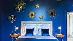 A bedroom with a blue wall, a white headboard, two bedside tables with lamps, and decorative sunburst mirrors.