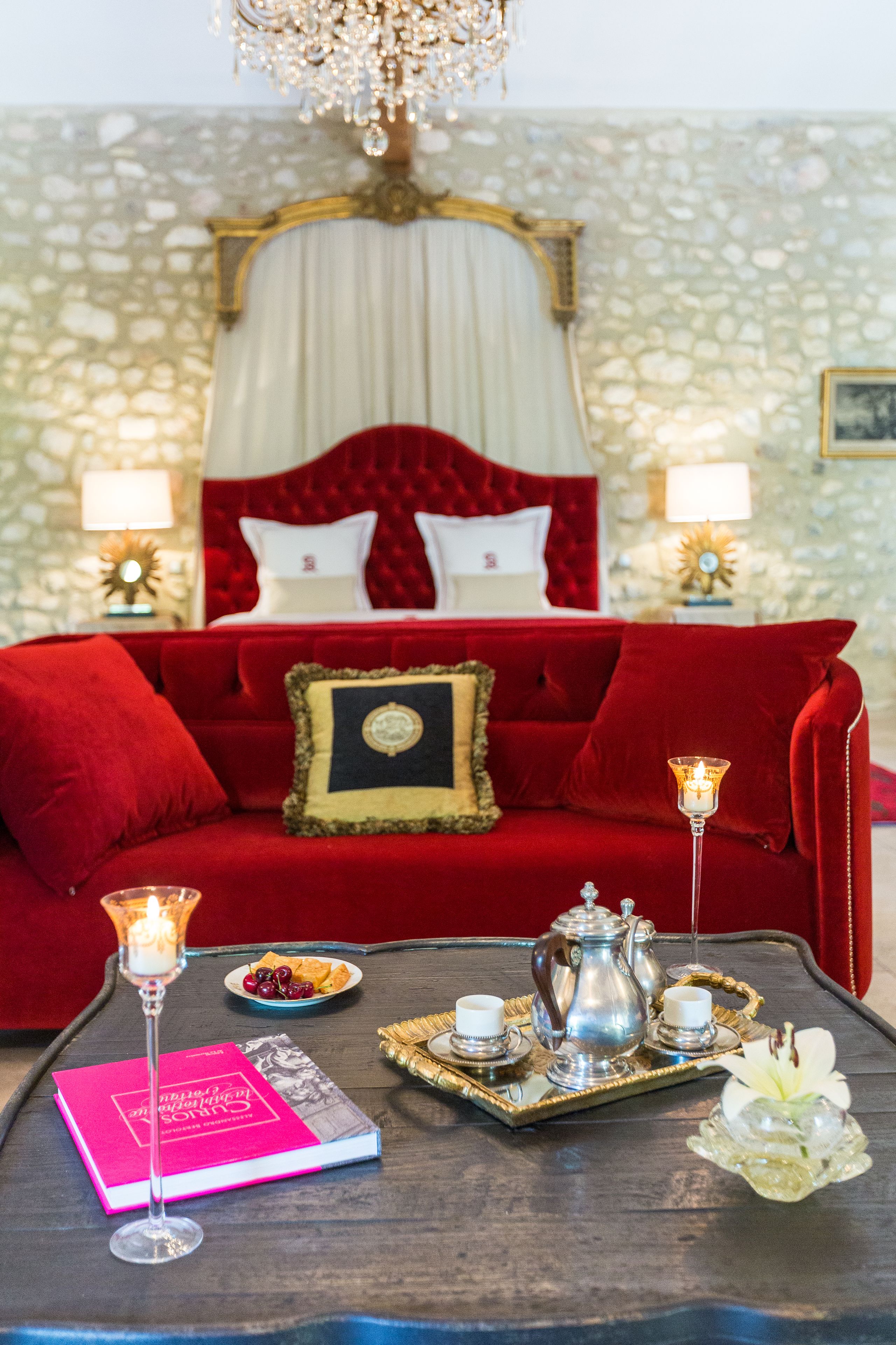 A red velvet sofa with a gold-framed headboard, a bedside table with a book and a candle, and a tray with a teapot and cups.