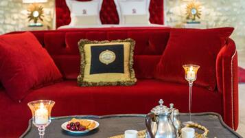 A red velvet sofa with a gold-framed headboard, a bedside table with a book and a candle, and a tray with a teapot and cups.