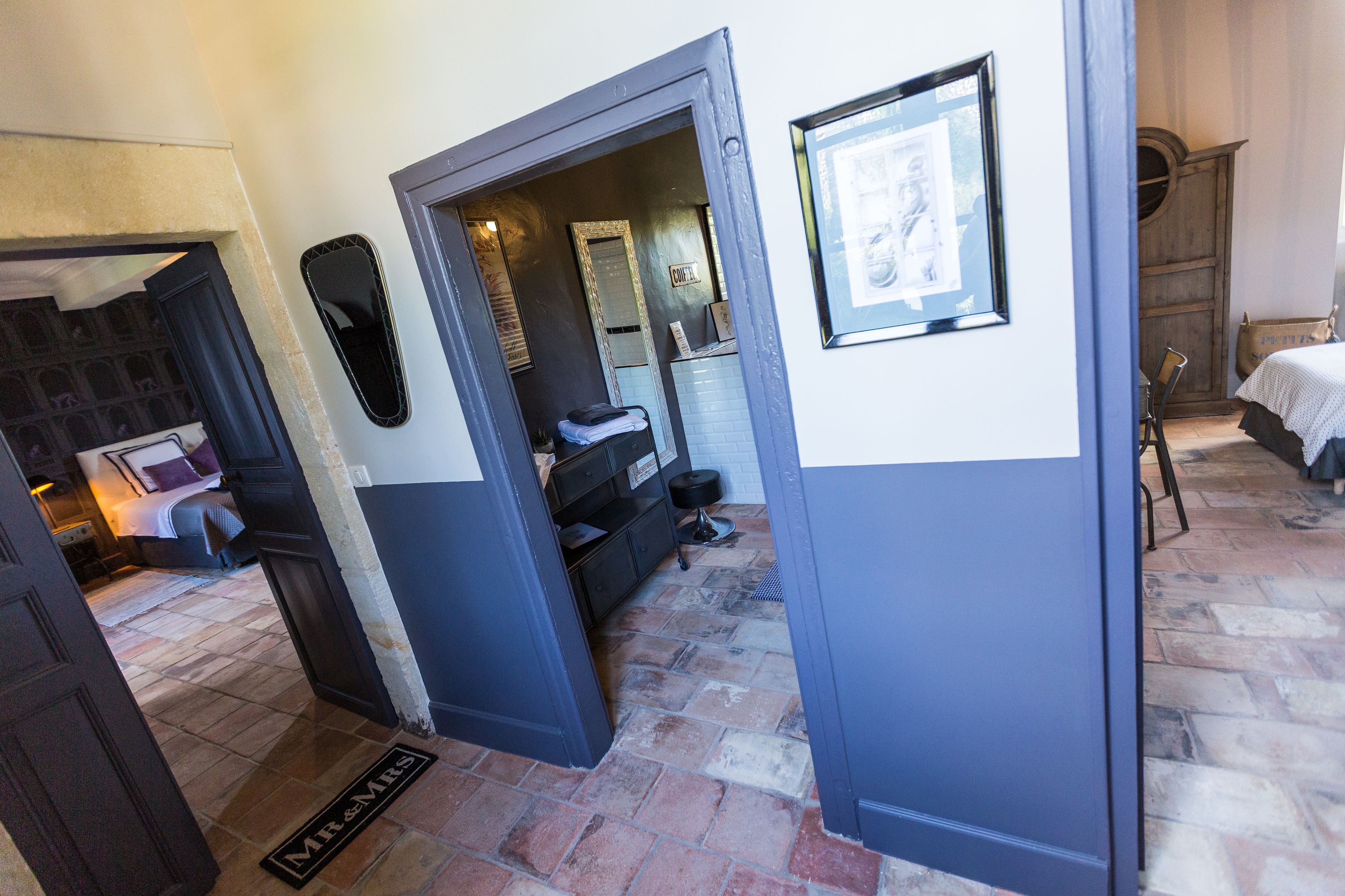A hotel room with a bed, a desk, and a chair. There is a door leading to another room.
