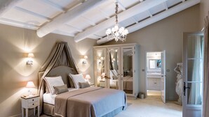 A bedroom with a canopy bed, bedside lamps, a chandelier, and a walk-in closet with a mirror.