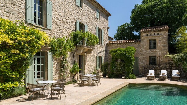 A stone building with a swimming pool, outdoor seating, and lush greenery.