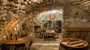 A cellar with stone walls, a wooden table with chairs, a wine rack, and barrels.