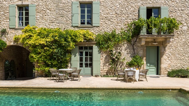 A stone building with a pool, outdoor seating, and shutters.