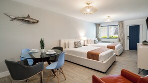 A modern hotel room with a glass dining table, two beds, a desk, and a large window with curtains.