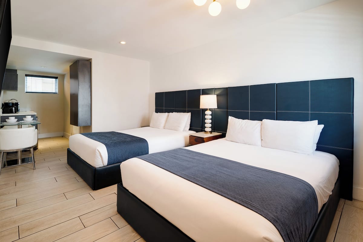 A hotel room with two beds, a desk, and a kitchenette.