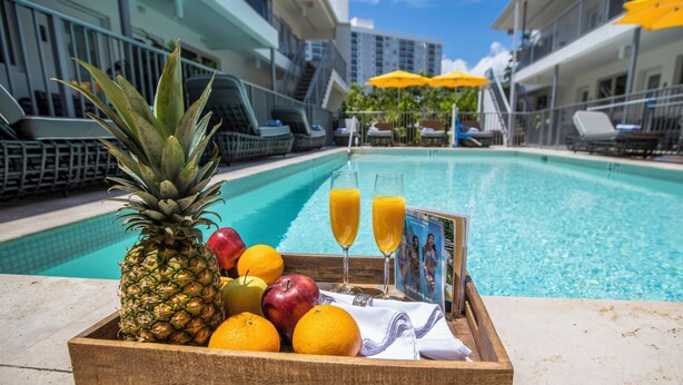 A wooden tray with fruits and two glasses of orange juice by a poolside.