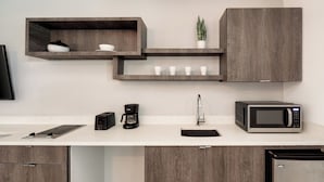 A modern kitchen with wooden cabinetry, a white countertop, a coffee maker, a microwave, and a sink.