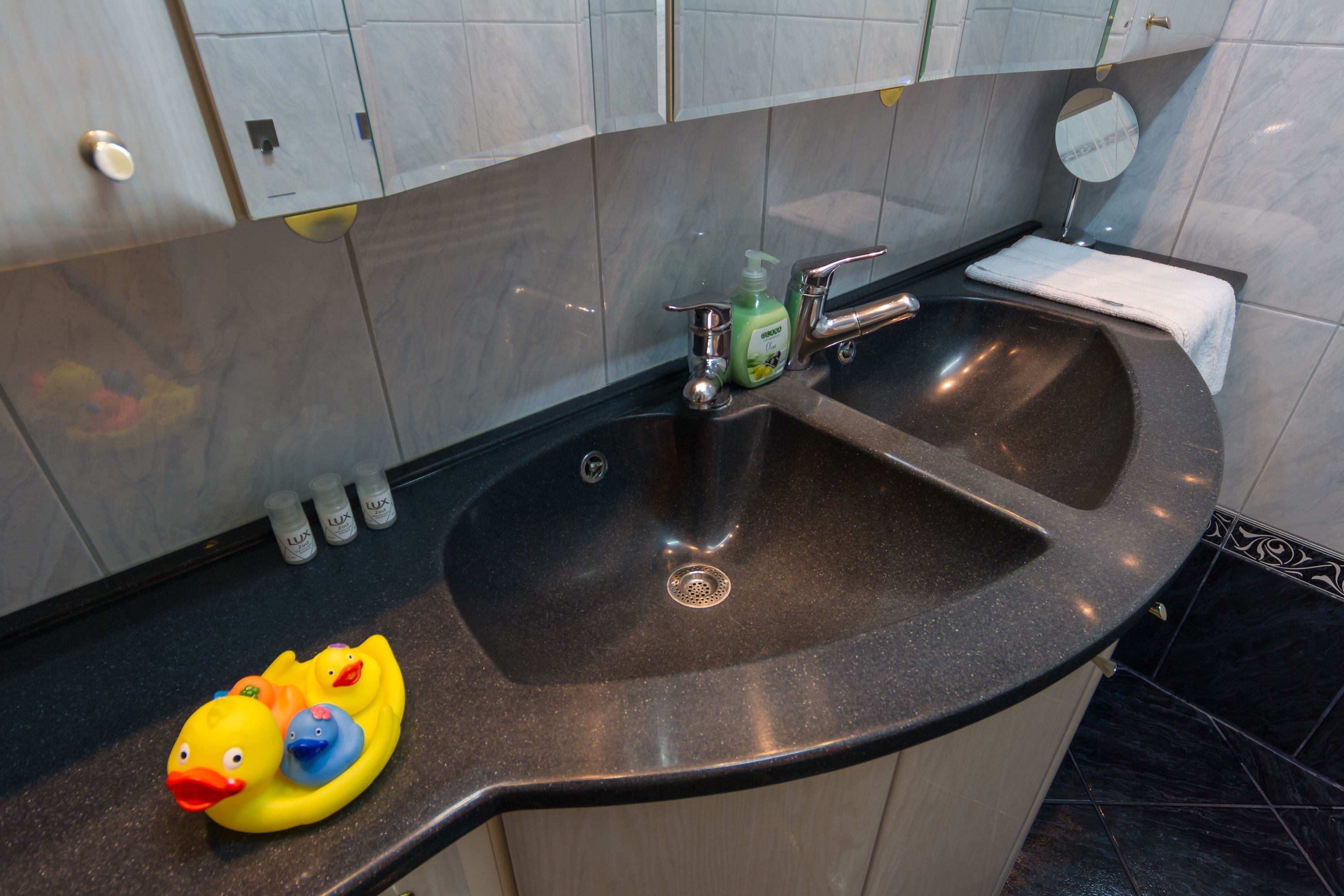 A bathroom with a black sink, a mirror, and a white towel. There are two rubber ducks on the counter.