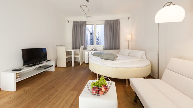 A modern hotel room with a white bed, a flat-screen TV, a desk, and a chair.