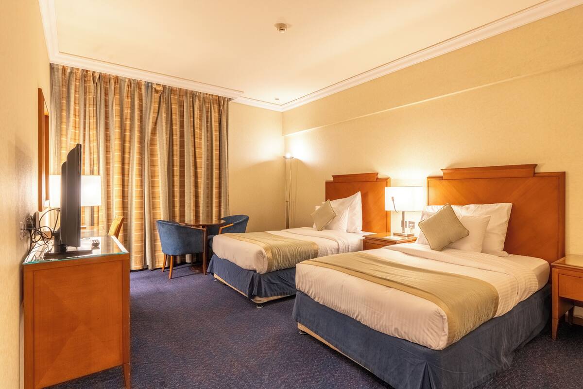 Une chambre d’hôtel avec deux lits, un bureau avec une télévision, une chaise et une lampe.