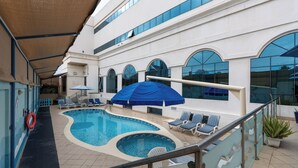 A pool area with two pools, lounge chairs, umbrellas, and a lifebuoy. - Lavender Hotel Sharjah (Sharjah)
