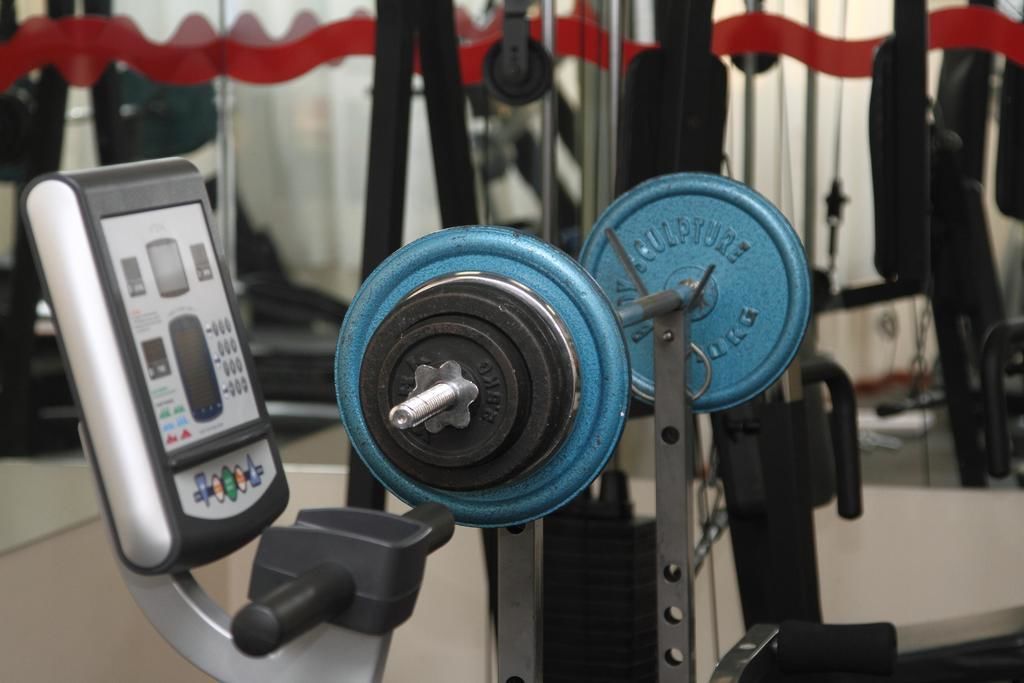 A weightlifting bench with a digital scale and a barbell with blue weight plates.