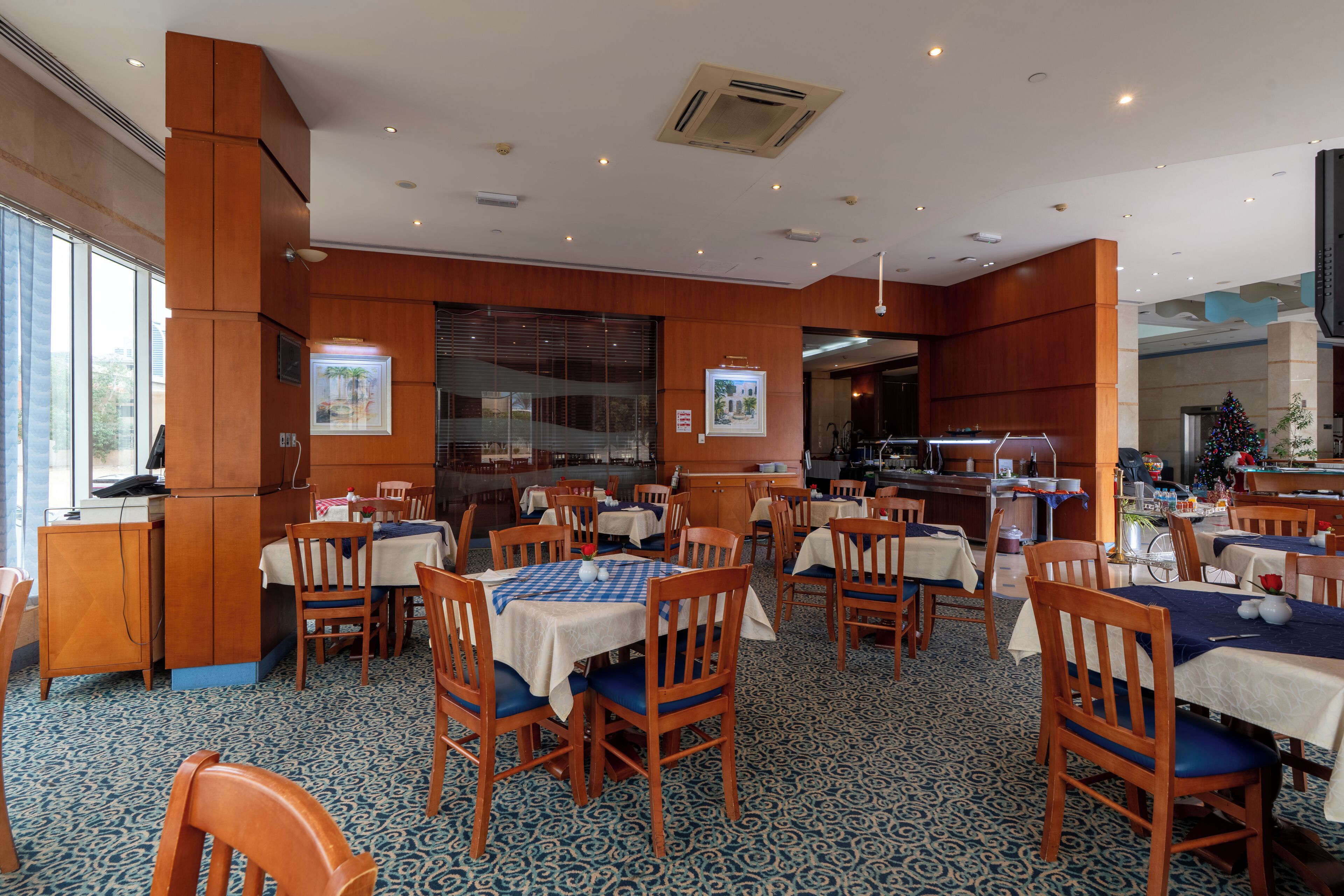 A hotel dining area with multiple tables and chairs, a large window, and a Christmas tree.