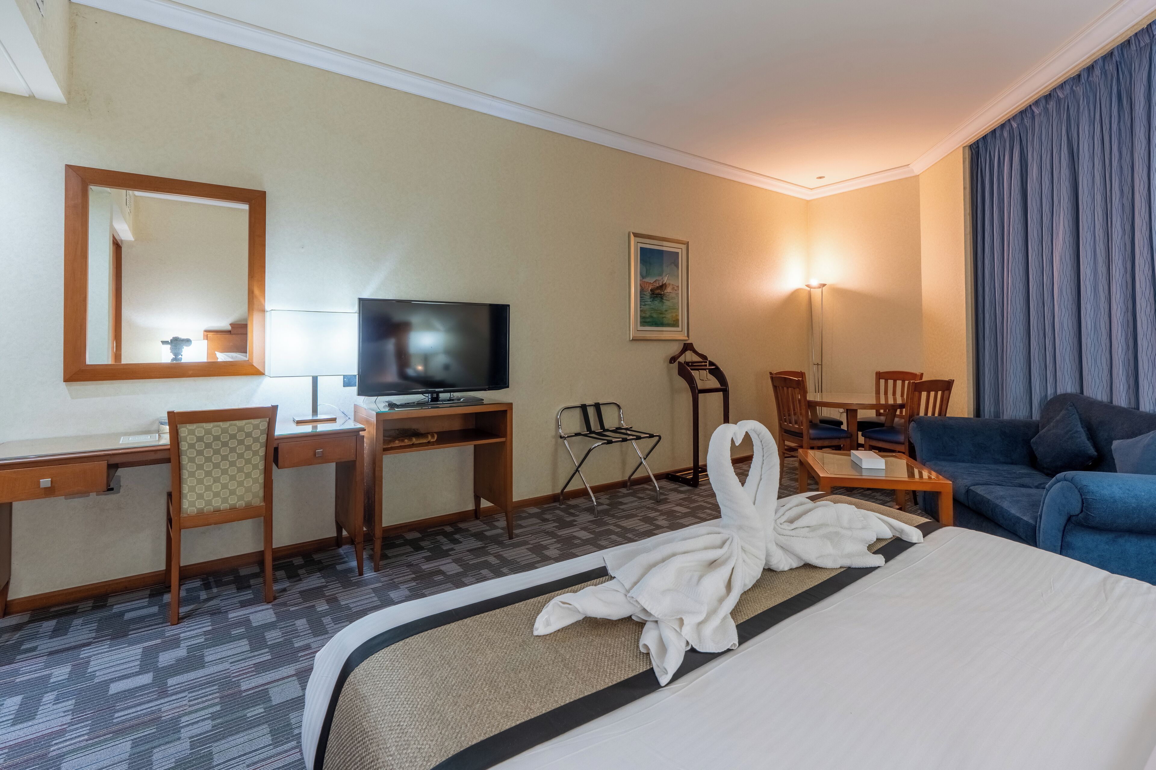 A hotel room with a bed, a desk with a television, a chair, a sofa, and a painting on the wall.