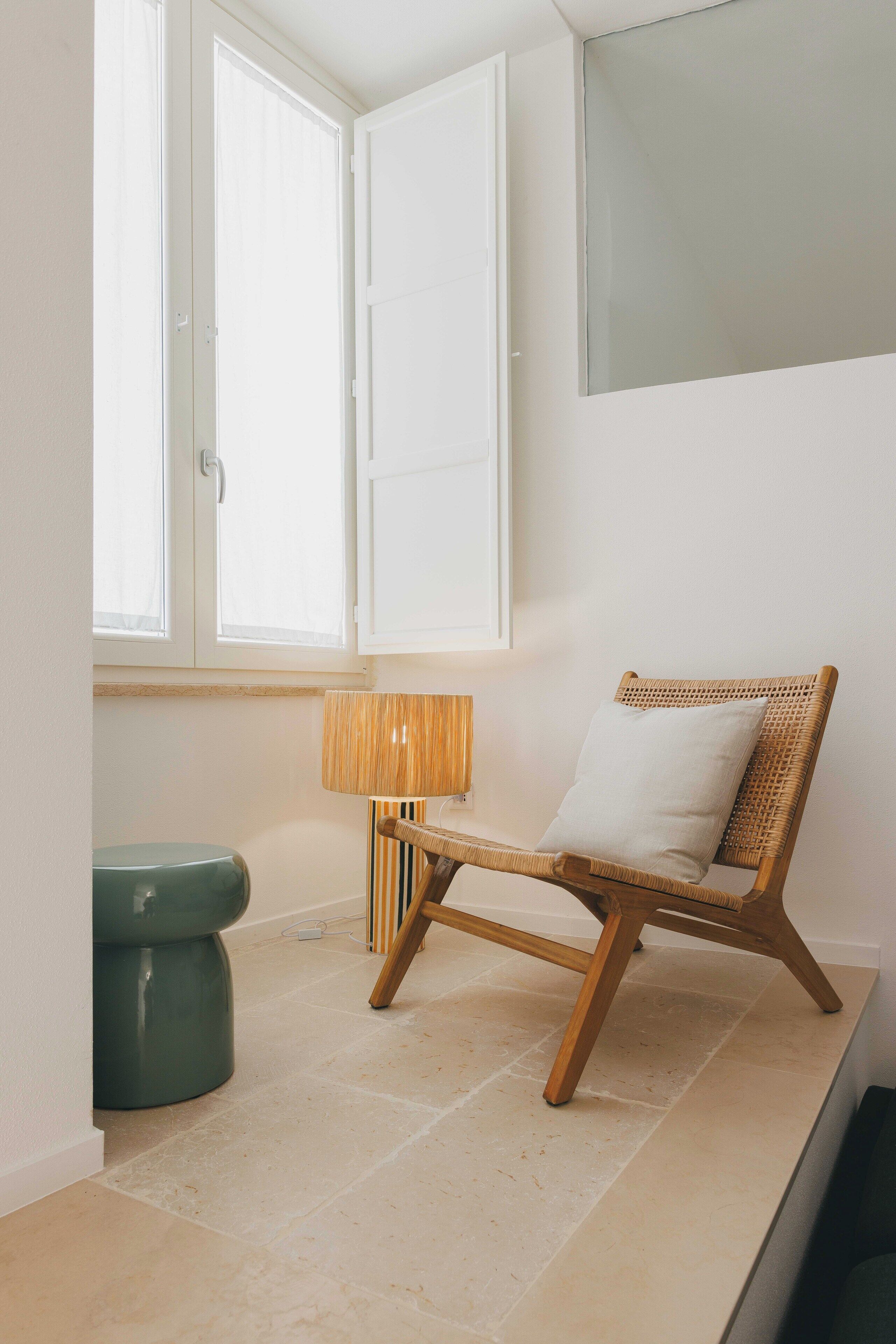 A room with a wicker chair, a green toilet, a striped lamp, and a window with white shutters.