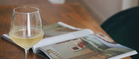 A wooden table with a wine glass, a pair of eyeglasses, and an open magazine.