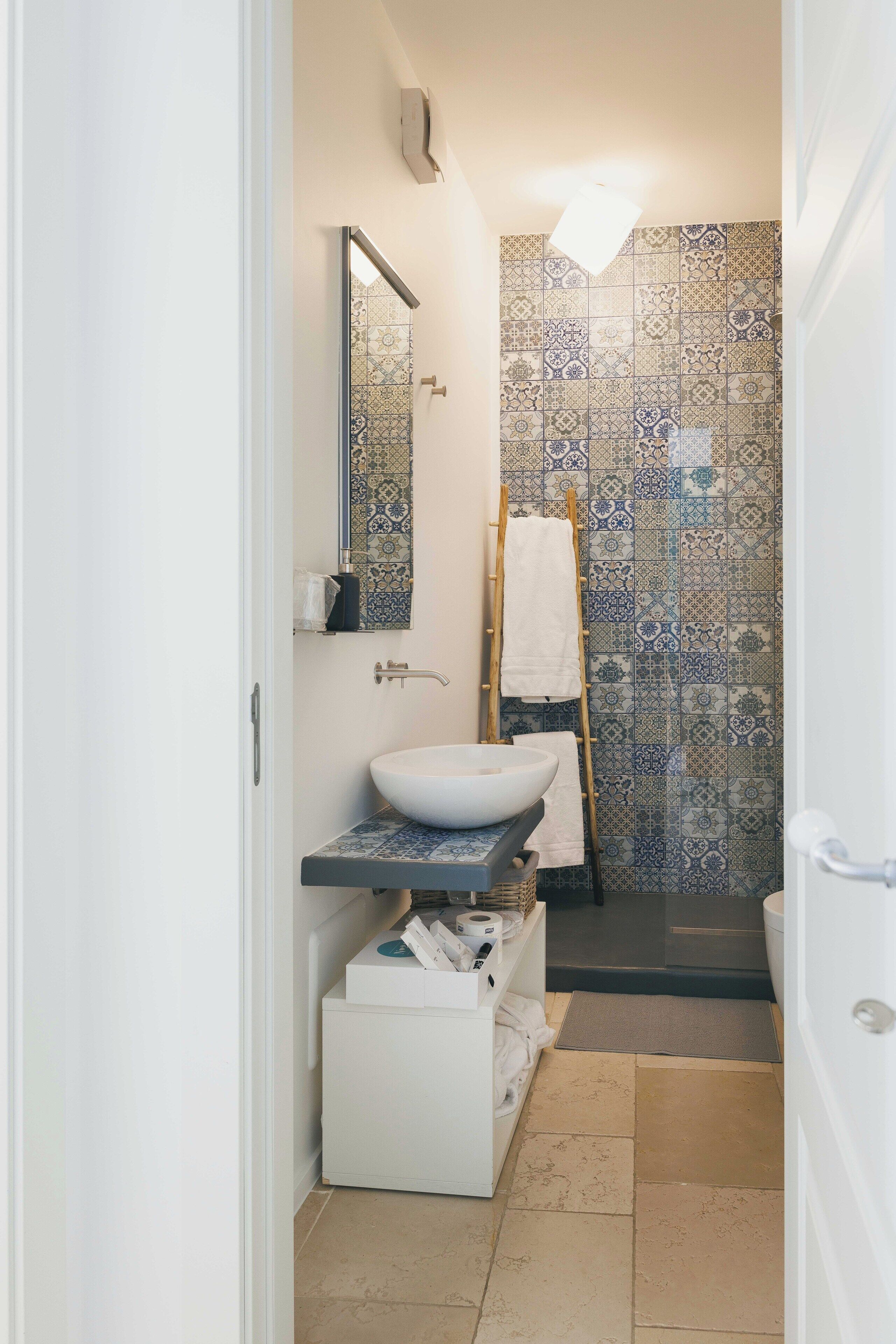 A bathroom with a white sink, a mirror, and a tiled shower wall.