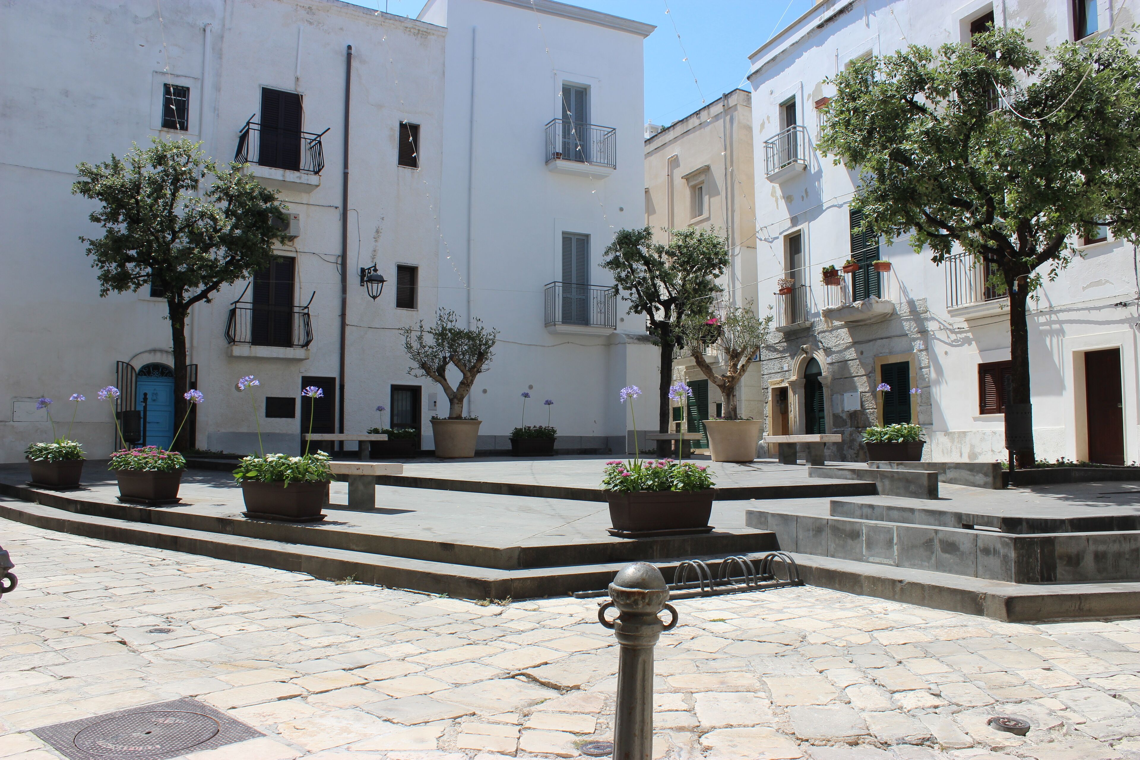 A courtyard with potted plants, stone steps, and white buildings with balconies.