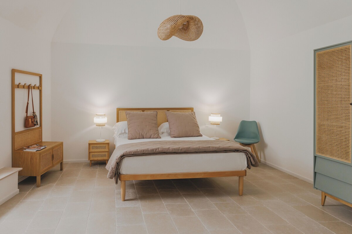 Un dormitorio con cama, mesitas de noche, lámpara colgante, silla y armario.