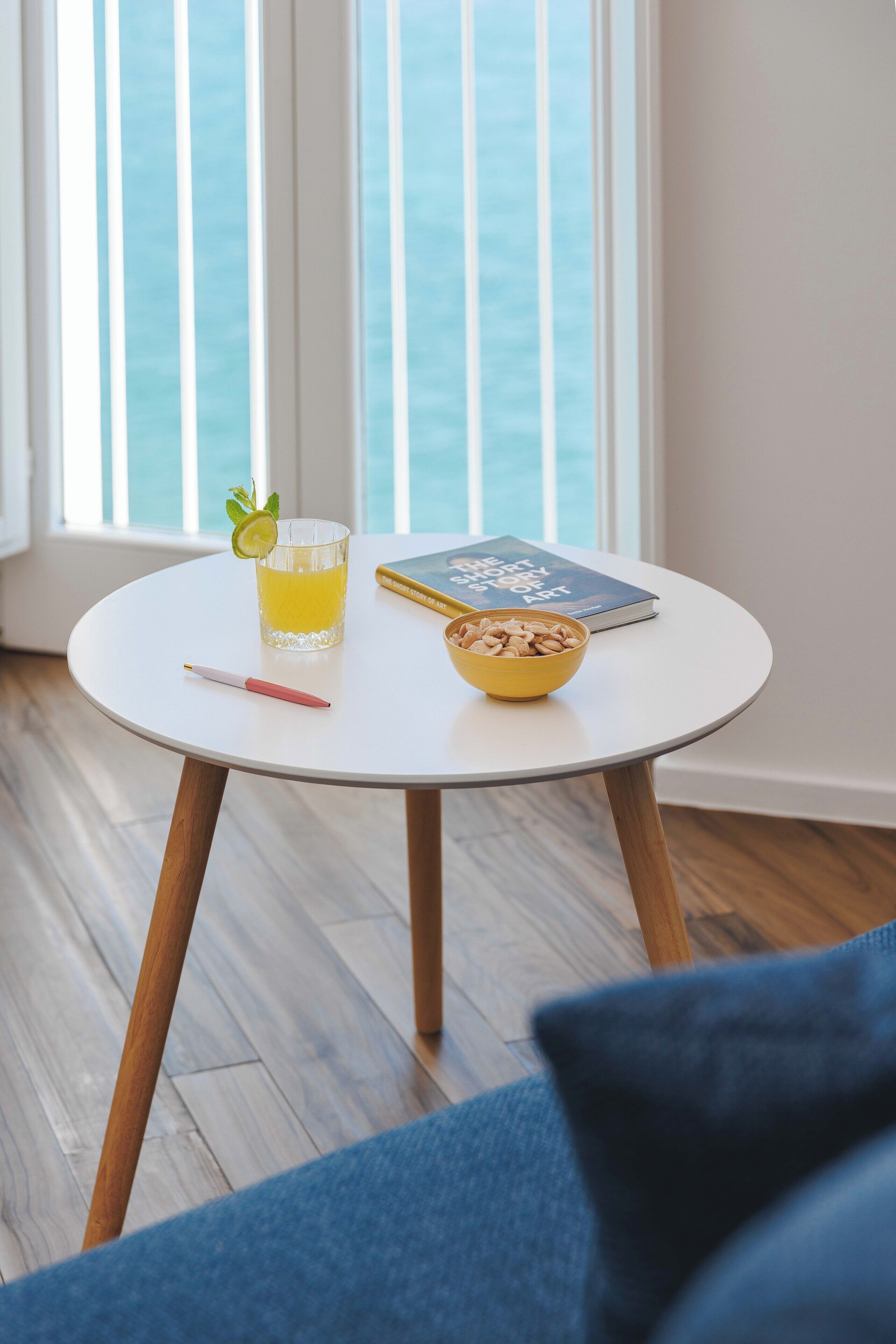 A round table with a glass of orange juice, a bowl of nuts, a notebook, and a pen.