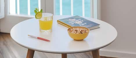 A round table with a glass of orange juice, a bowl of nuts, a notebook, and a pen.