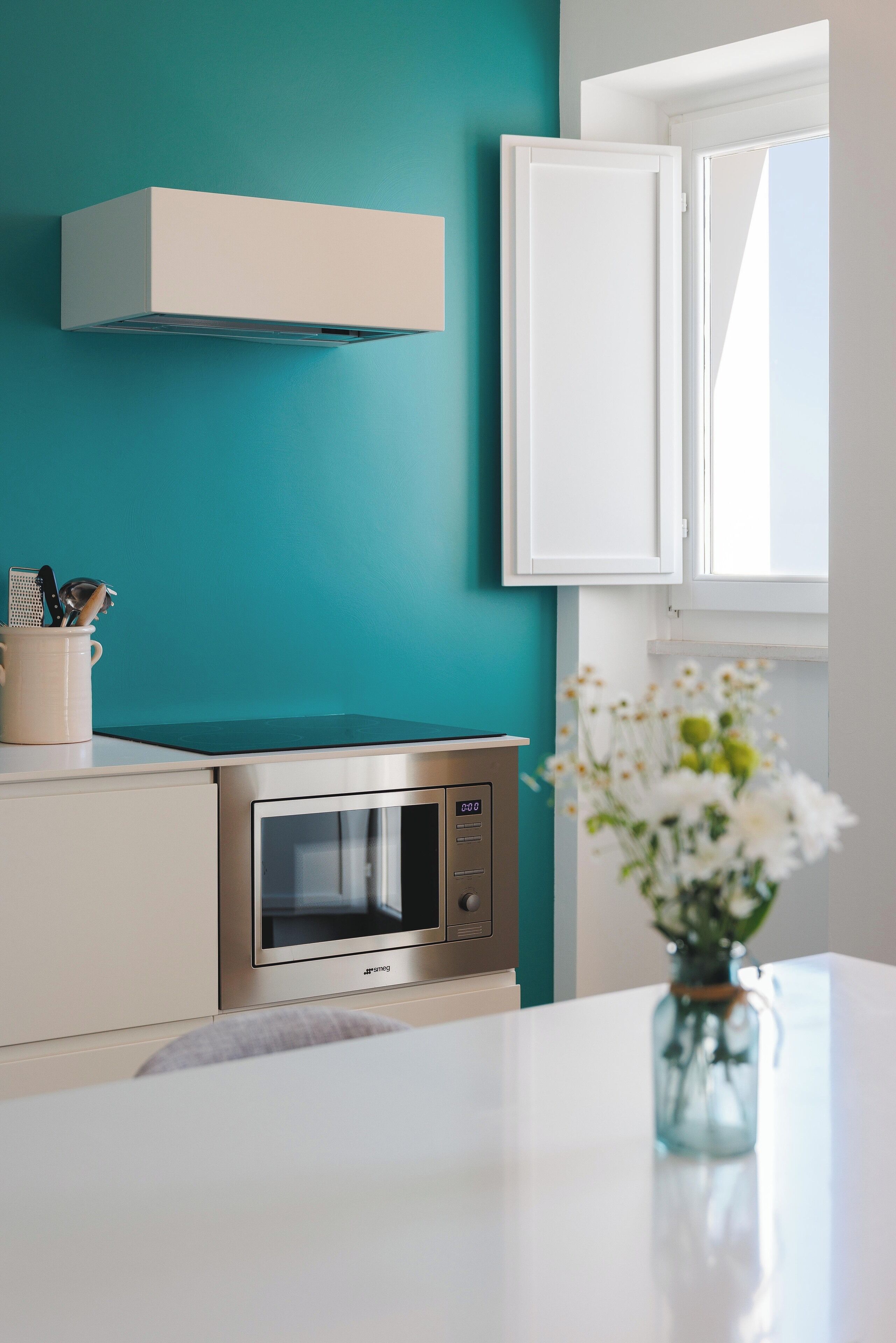 A kitchen with a teal wall, white cabinets, a stainless steel oven, and a white countertop.