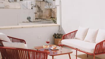 Una terraza en la azotea con un sofá blanco, sillas de mimbre rojas y una mesa con una cesta y una copa de vino.
