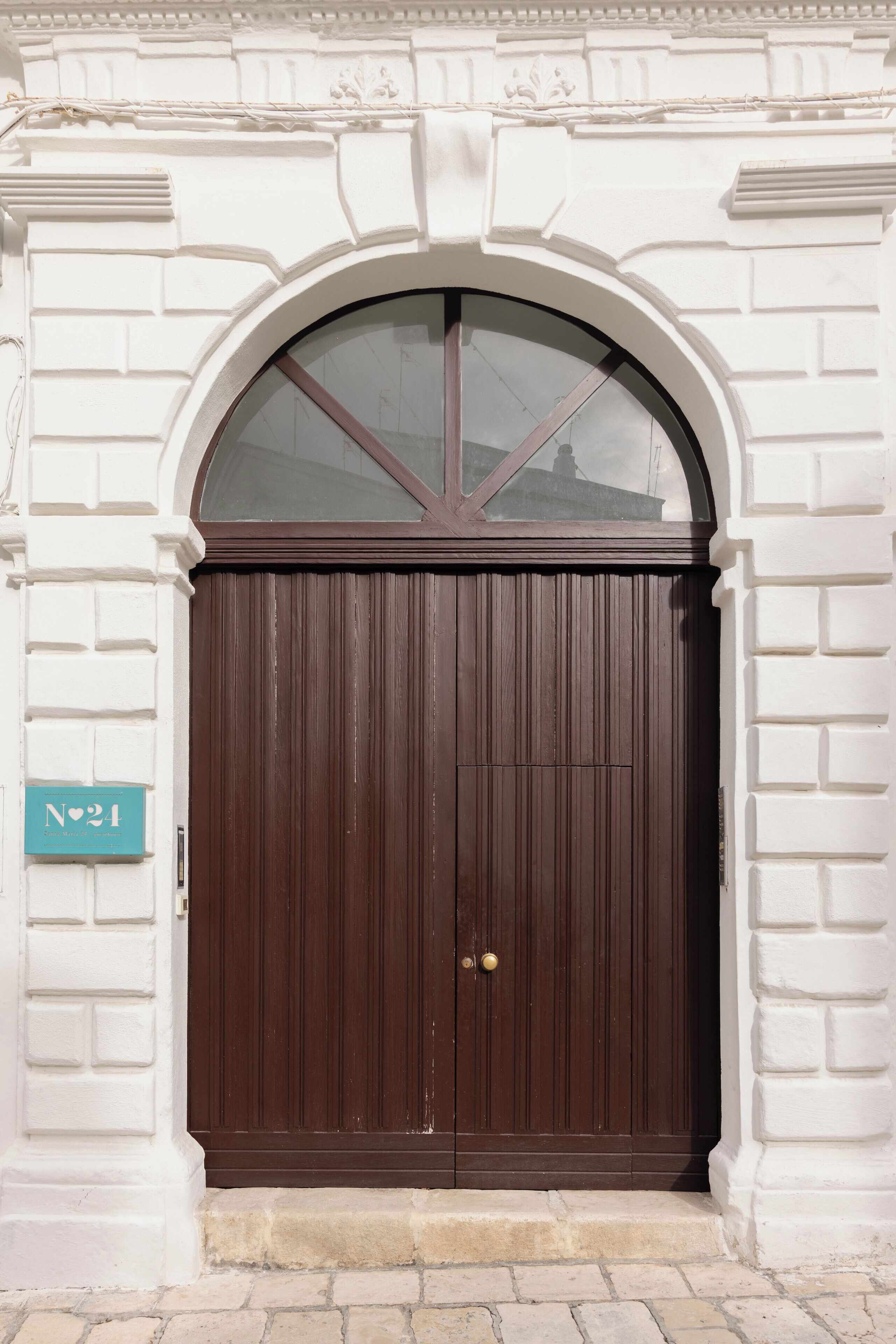 A large, dark brown wooden door with a glass panel above it, set in a white brick wall with a decorative arch.