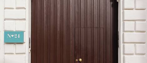 A large, dark brown wooden door with a glass panel above it, set in a white brick wall with a decorative arch.