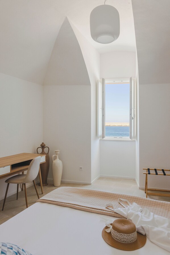 Un dormitorio con cama, escritorio, silla, ventana con vista al mar y una lámpara colgante.