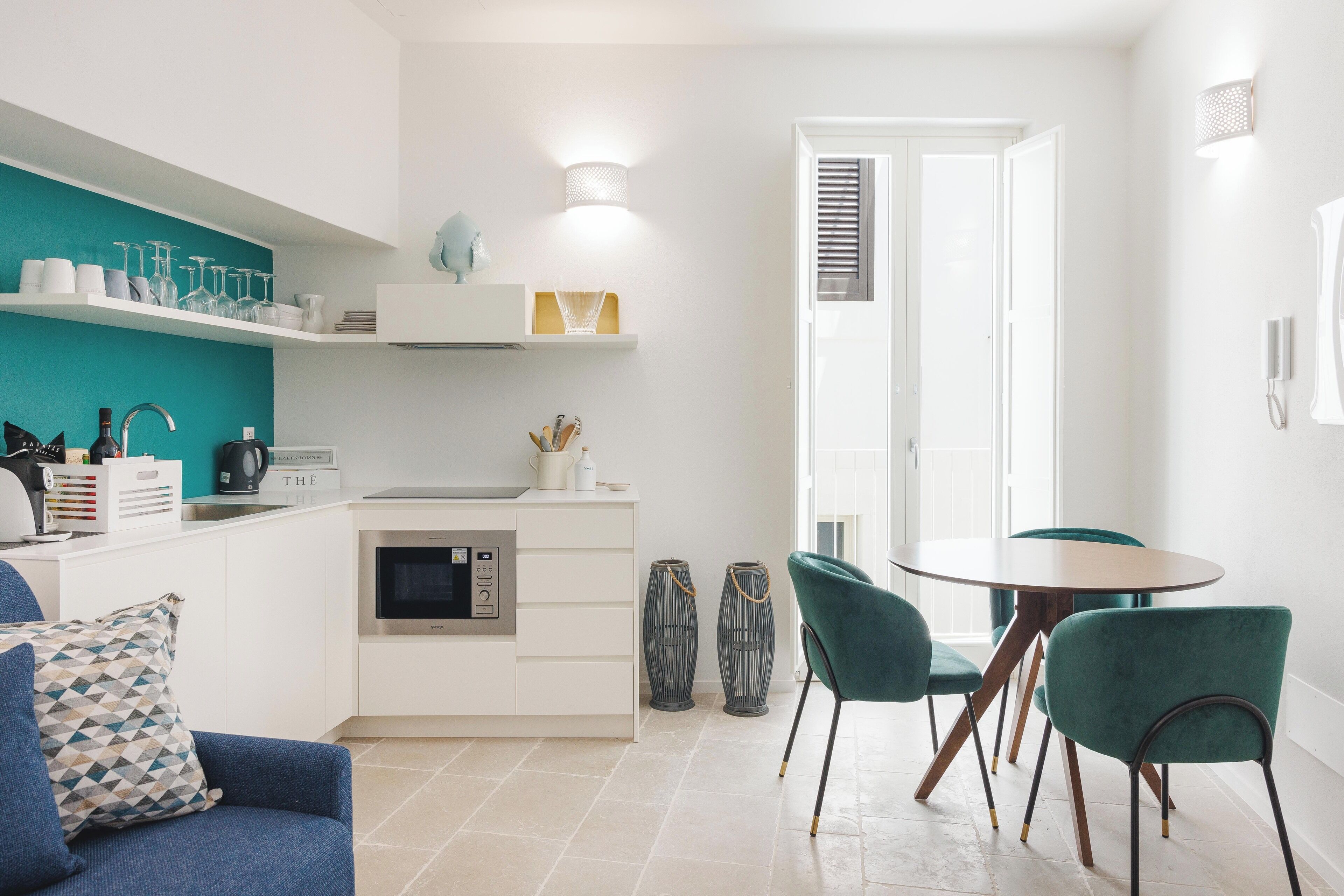 A modern kitchen with white cabinets, a teal backsplash, and a dining area with teal chairs.