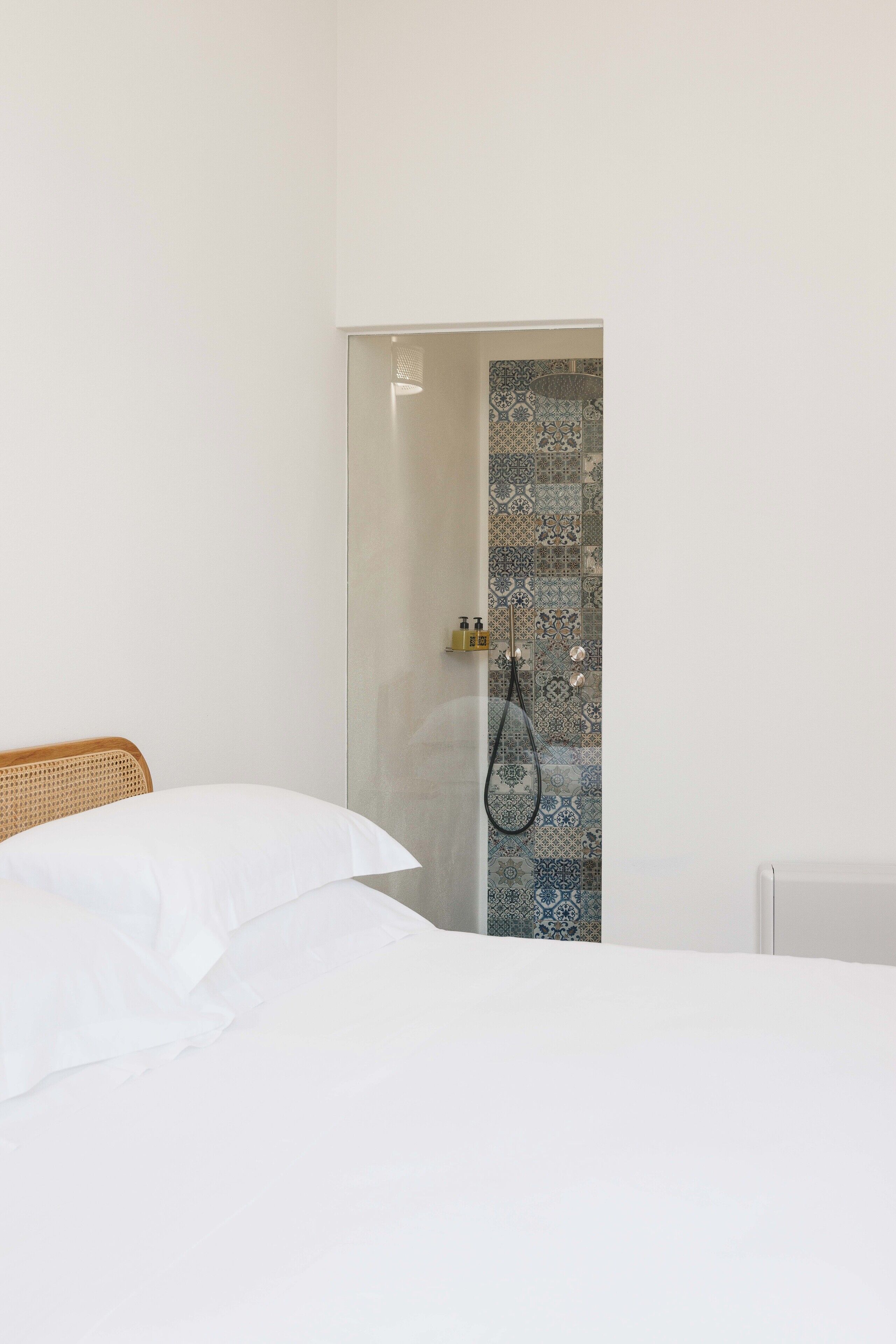 A bedroom with a bed, a shower area with patterned tiles, and a white wall.
