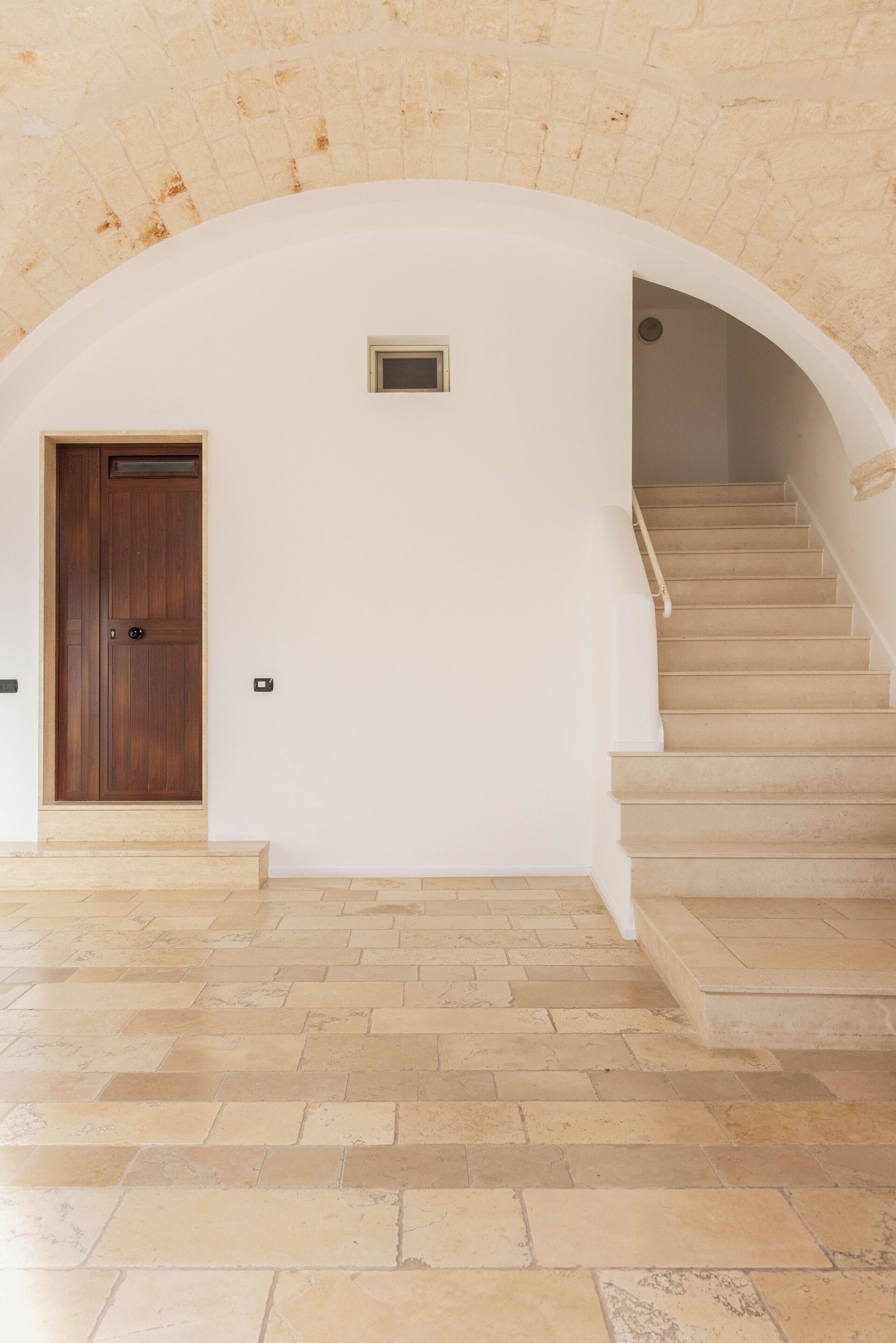 Eine Treppe mit einer Holztür am Fuß, die zu einem Zwischenpodest mit einem kleinen Fenster führt.