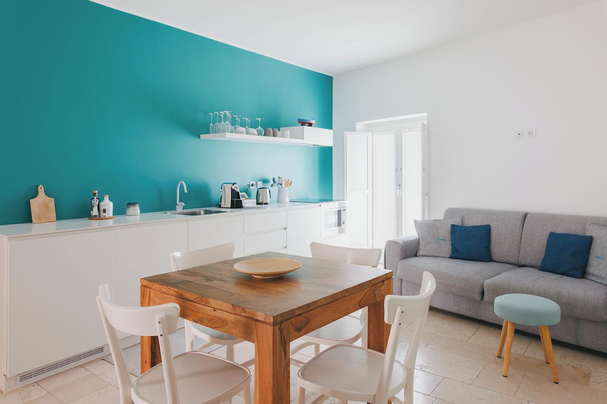 Une cuisine moderne avec des meubles blancs, un mur d’accent de couleur turquoise et une table à manger en bois avec des chaises.