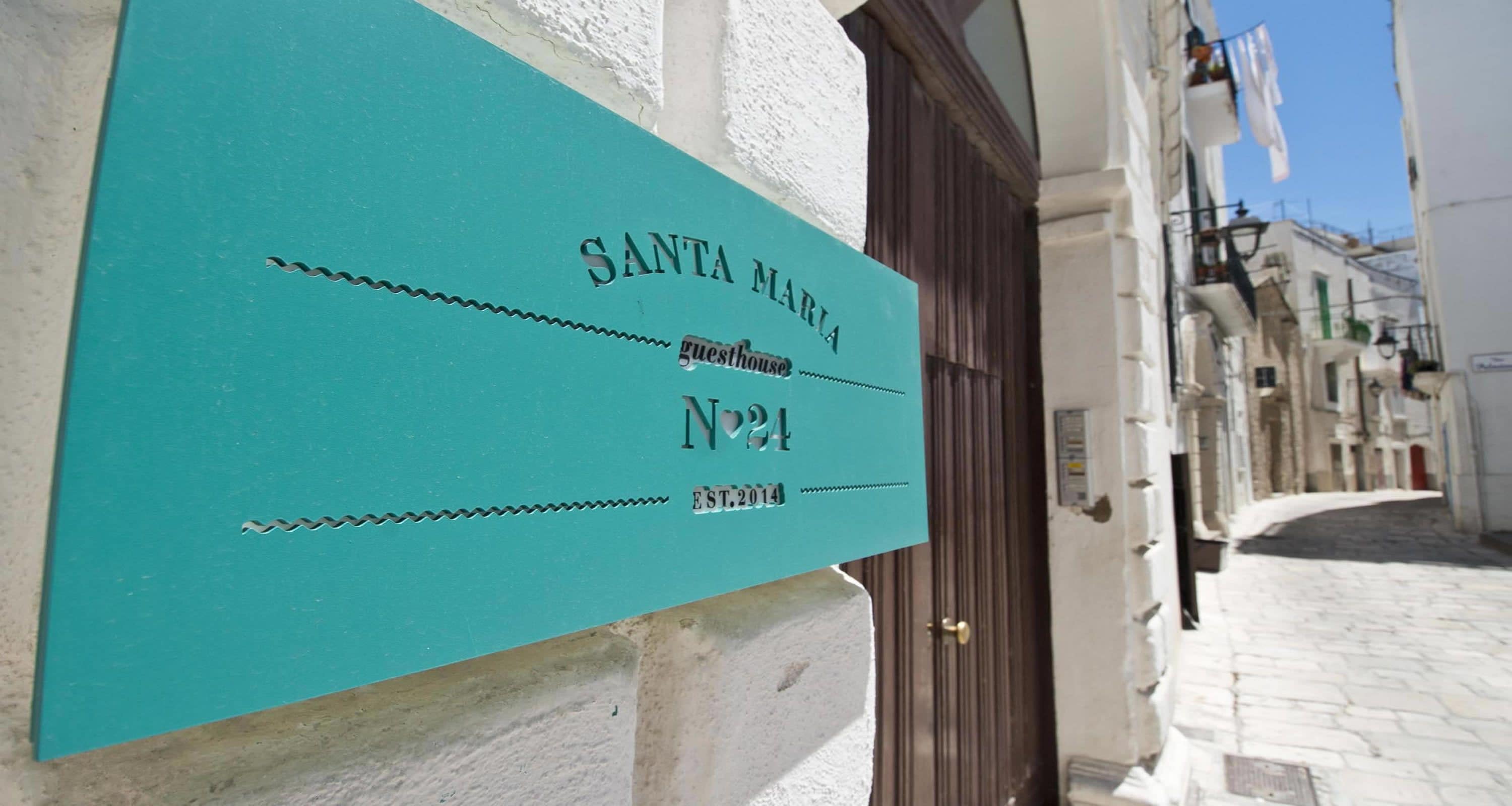 A turquoise sign for Santa Maria guesthouse, No. 24, established in 2014, on a building's exterior wall.