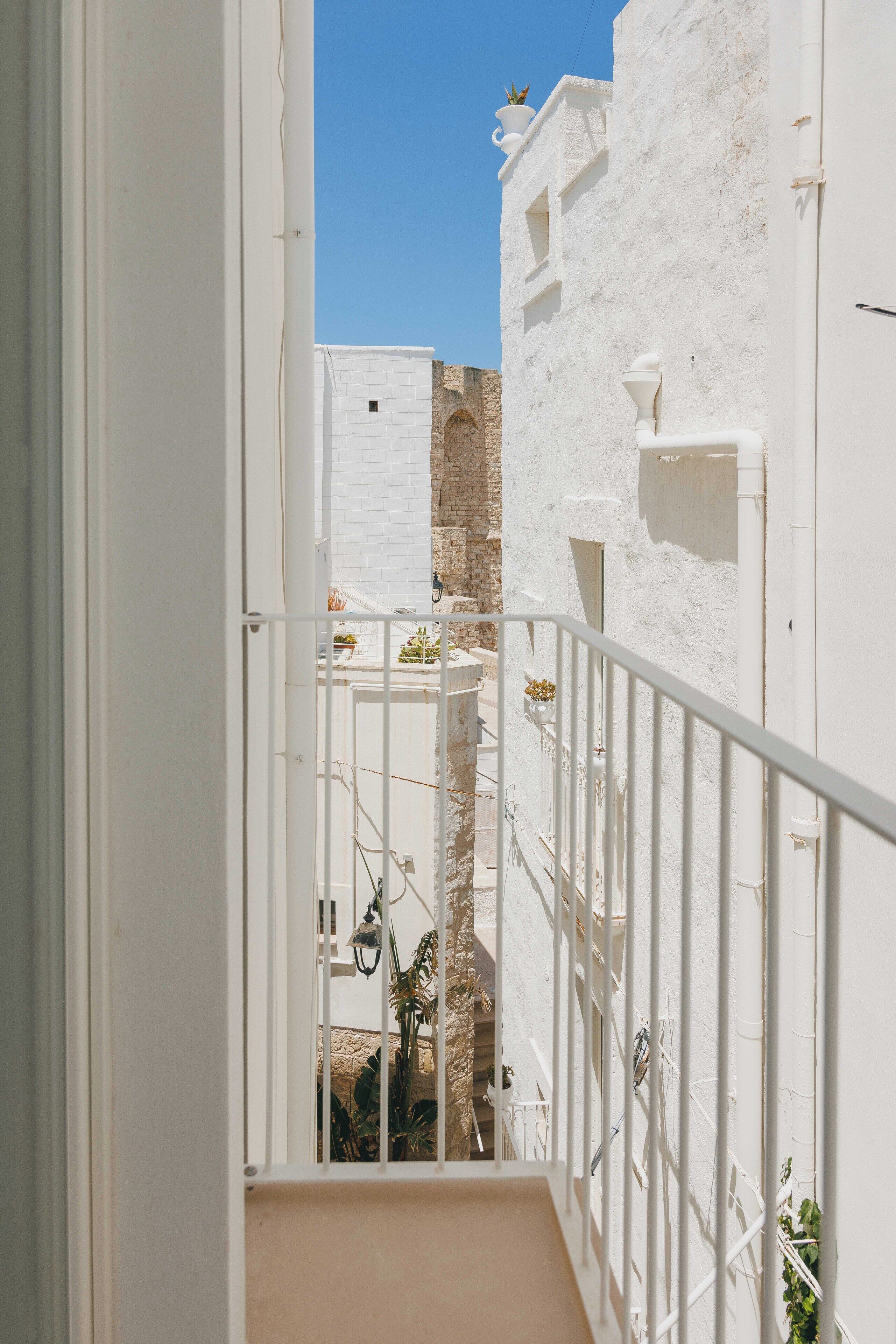 A narrow, white-walled corridor with a metal railing, leading to a staircase.
