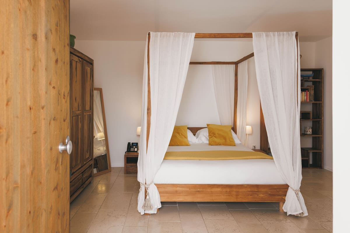 Un lit à baldaquin avec des rideaux blancs, une tête de lit en bois et un plaid jaune.