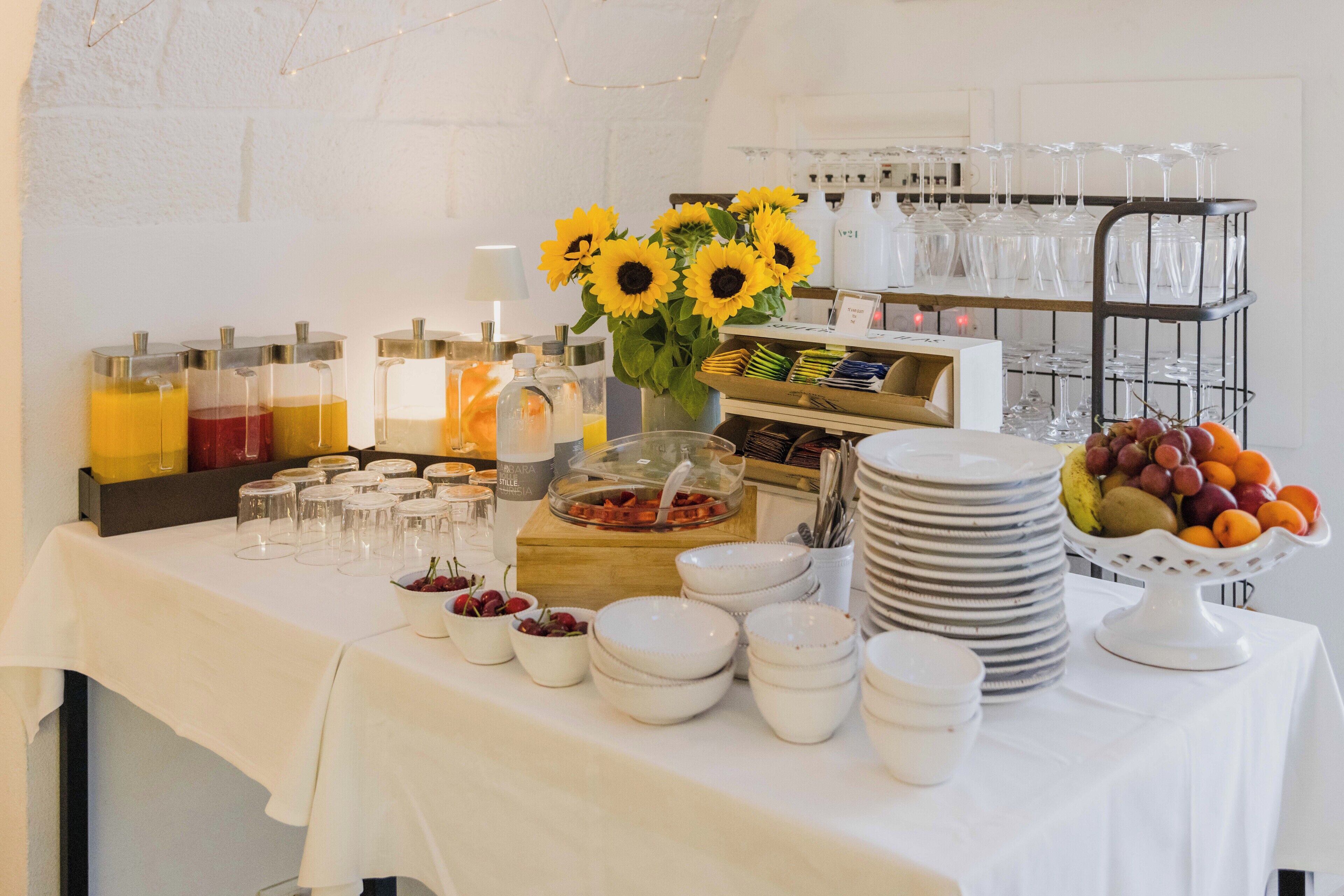 A buffet table with various food items, glassware, and a vase of sunflowers.