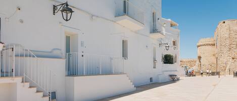 A white building with a staircase, a balcony, and a stone wall in the background.
